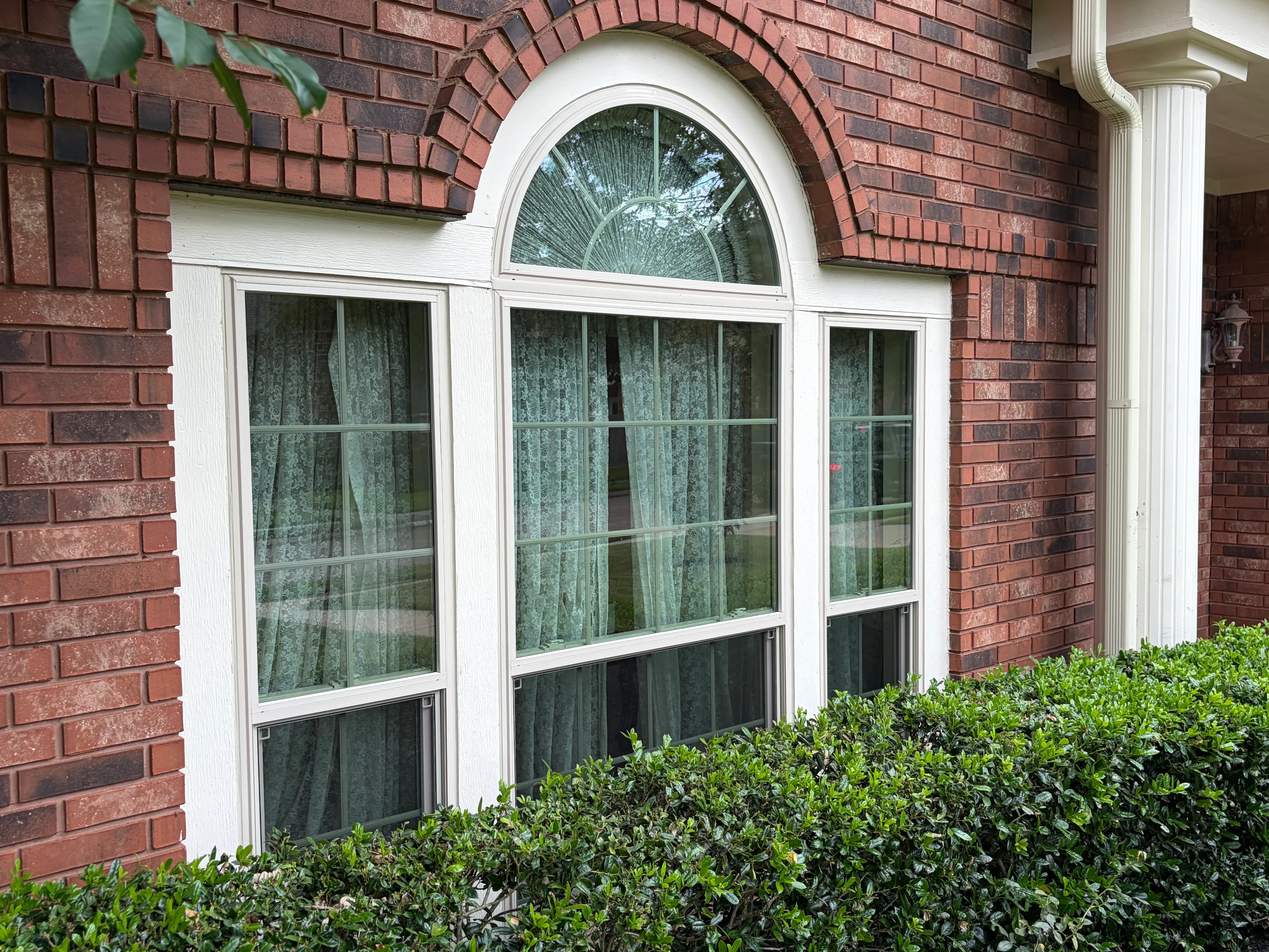 White-framed arched transom window with three casement windows installed in red brick exterior wall