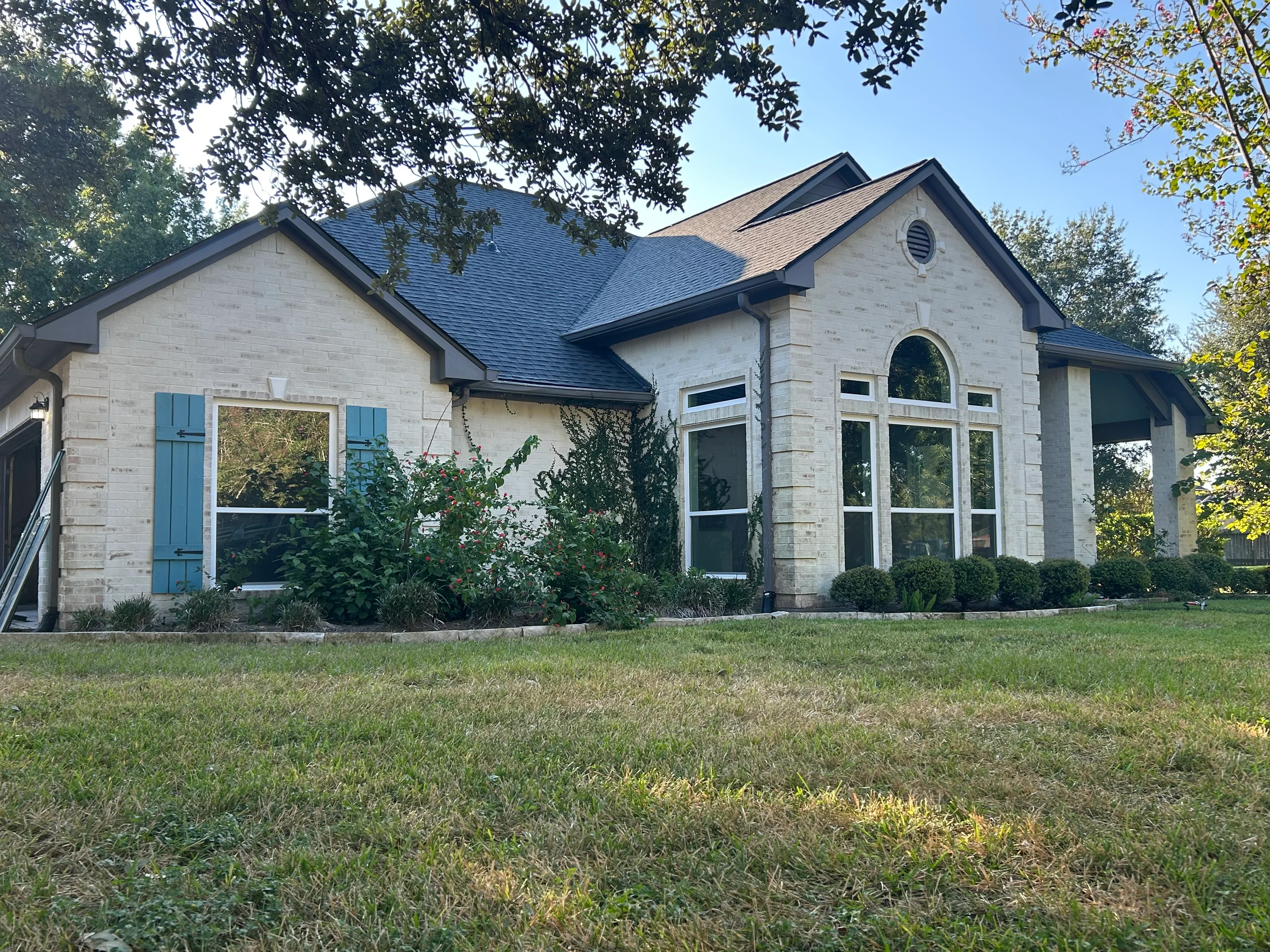 White brick home with new arched and rectangular windows, dark trim, blue-gray roof